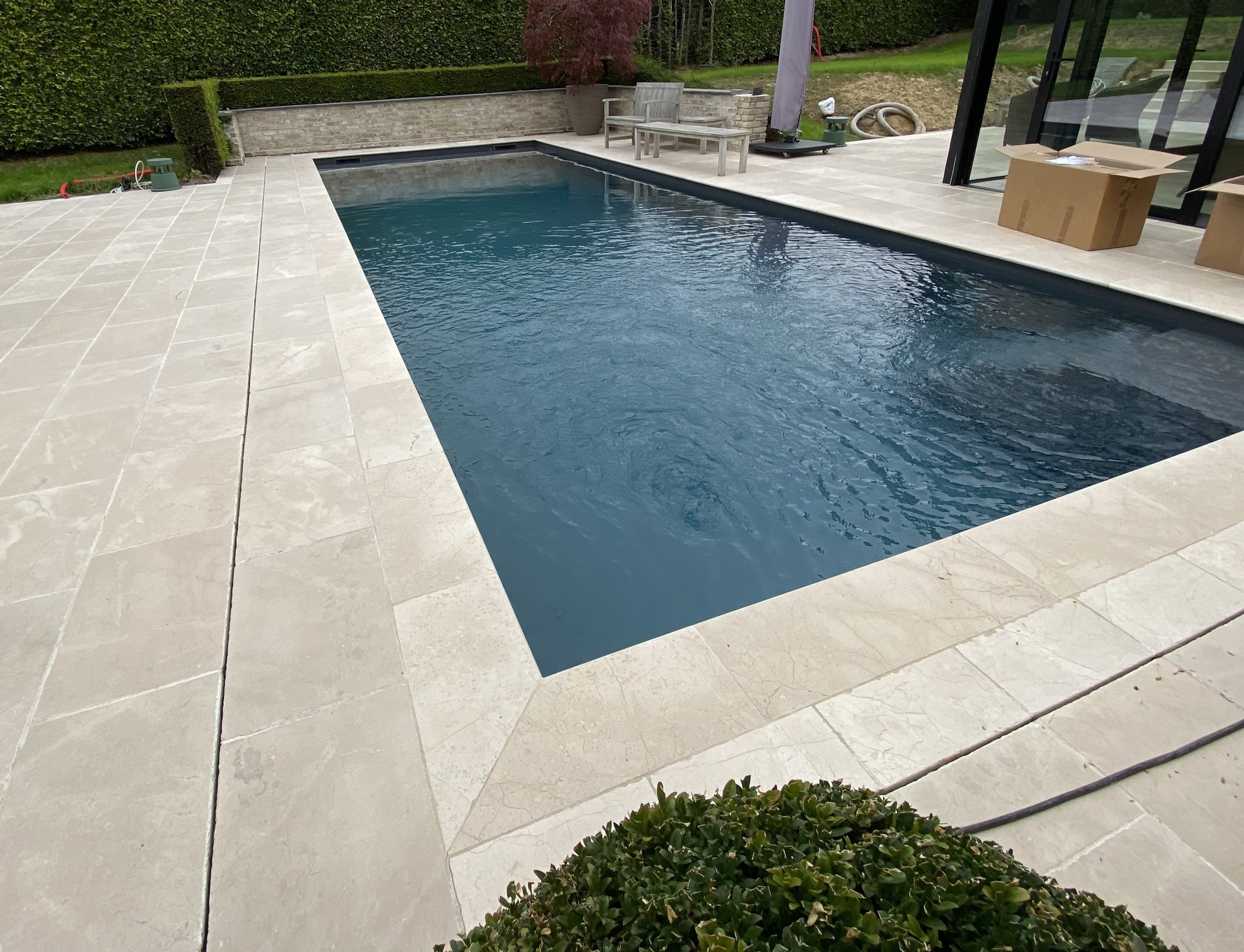 Zwembad met automatisch zwembadrolluik en houten ombouw naast grijze steenboord